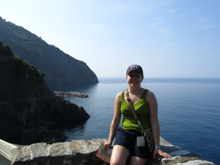 a woman is sitting on the side of a hill next to the ocean