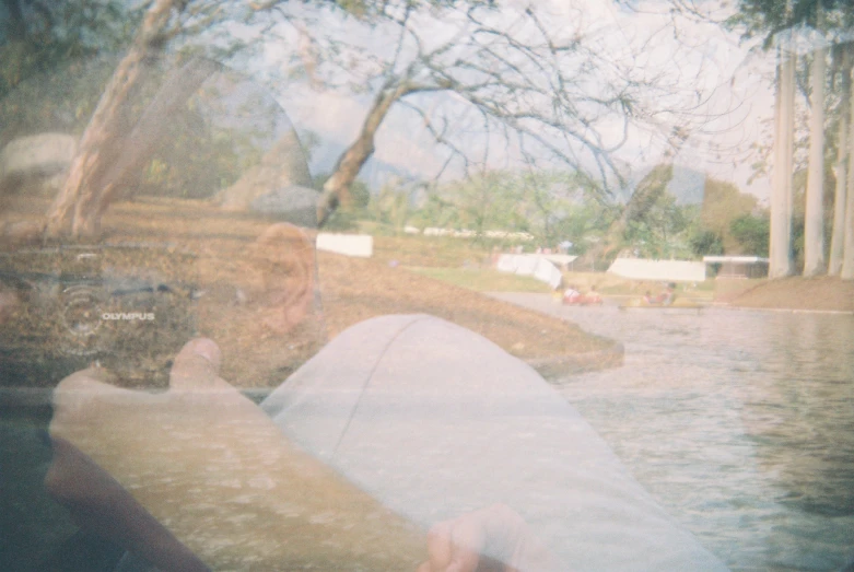 a boy is sitting next to the river taking a selfie