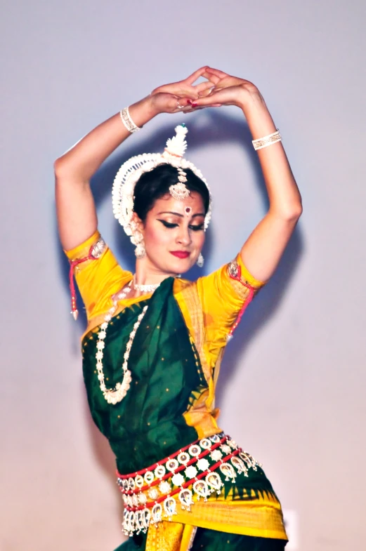 a girl in a green and yellow outfit performing an indian dance