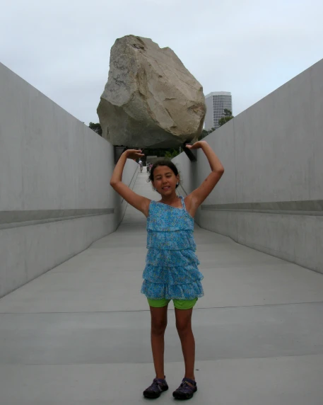 a girl in a blue dress carrying a rock over her head