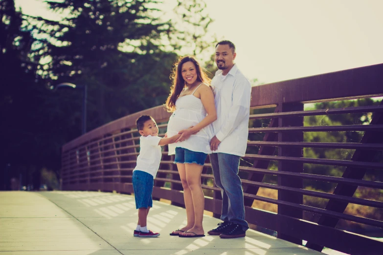 a woman, man and child holding hands by a bridge