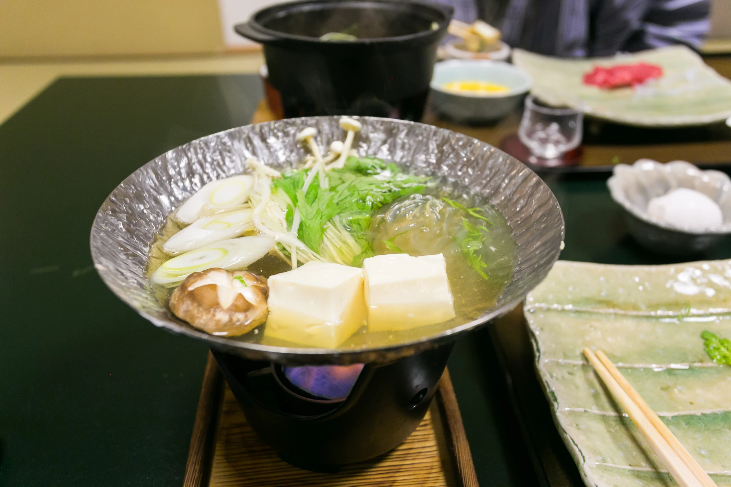 a bowl of soup, potatoes, lettuce, and other food items sit on a table
