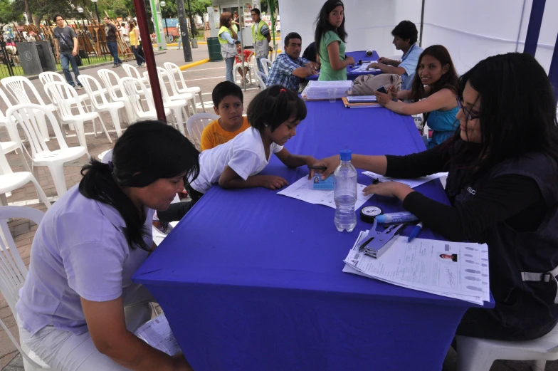 a group of children sit at a table with white chairs