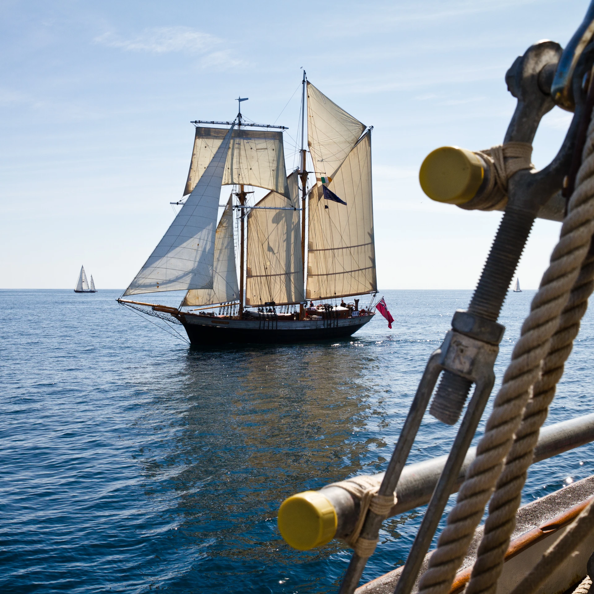 sail boat sails out on the water next to a ship