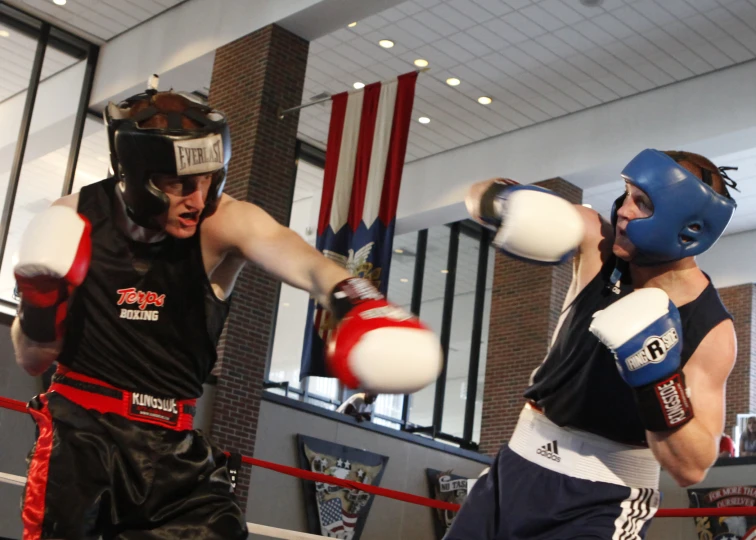 two people fighting in an indoor ring wearing protective gear