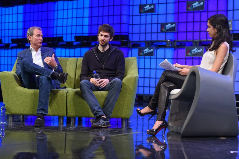 three people sitting on two chairs in front of a blue screen