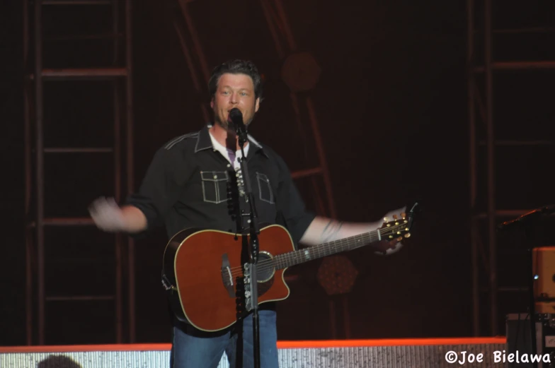 a man holding his guitar standing on stage