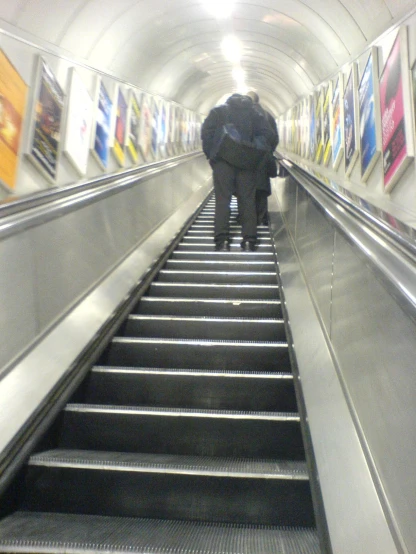 two people walking down an escalator with a umbrella