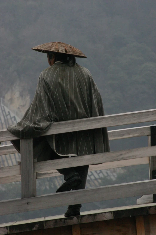 man sitting on the end of a bridge in front of mountains