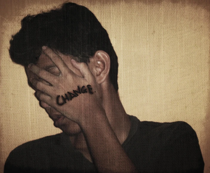 a young man is covering his face with the word change painted on his hands