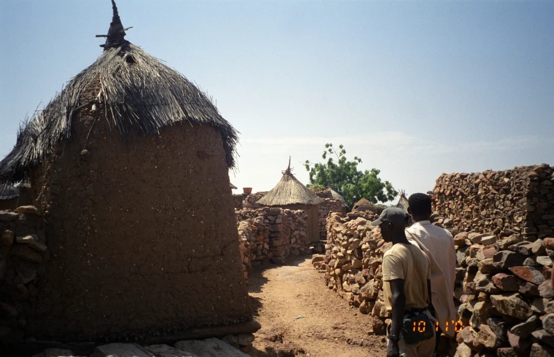 two men walk along the side of a stone house