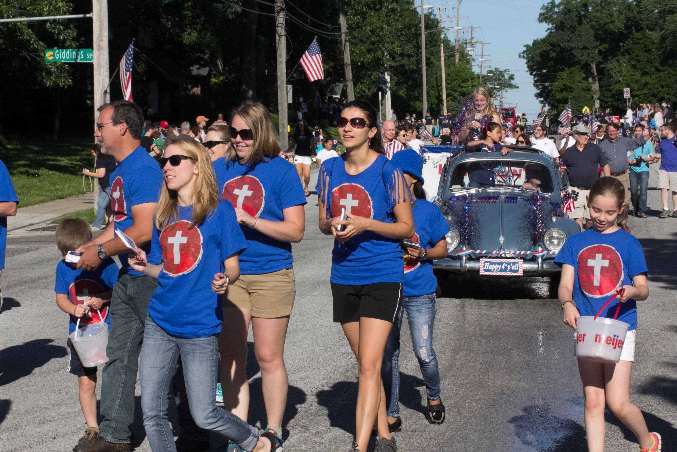 many people are walking with patriotic flags and cars on a city street