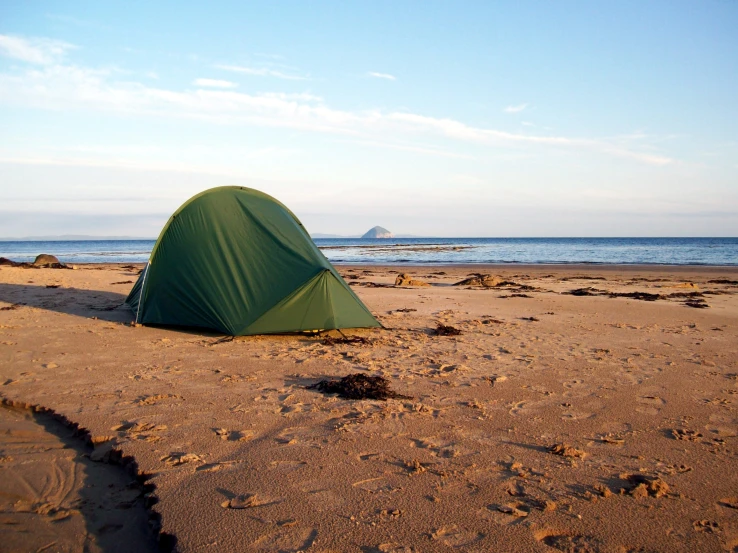 there is a green tent on the beach next to the ocean