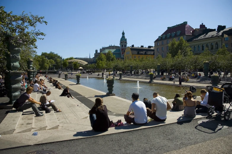 people sit near a small pond in a city park