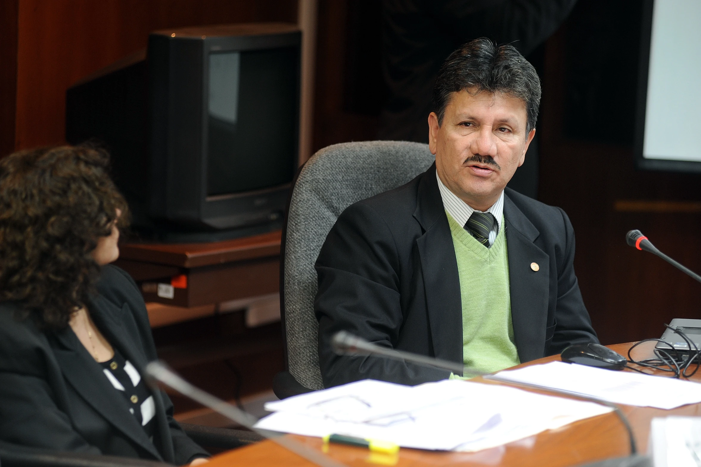 a man sits in front of a microphone as a woman looks on