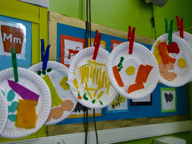 paper plates with paper pictures hanging from a wall