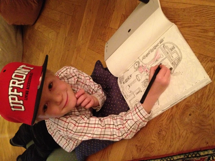 a boy with his hand in his mouth sitting on the floor drawing a page