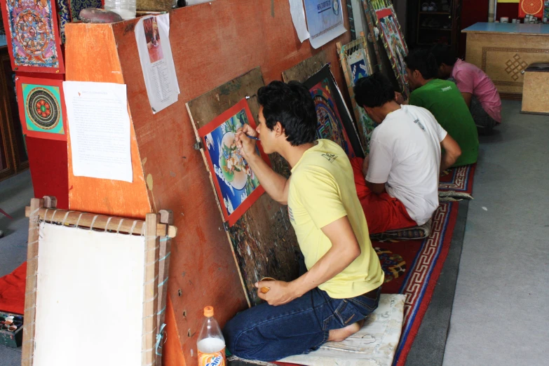 man working on painting while two men seated in front