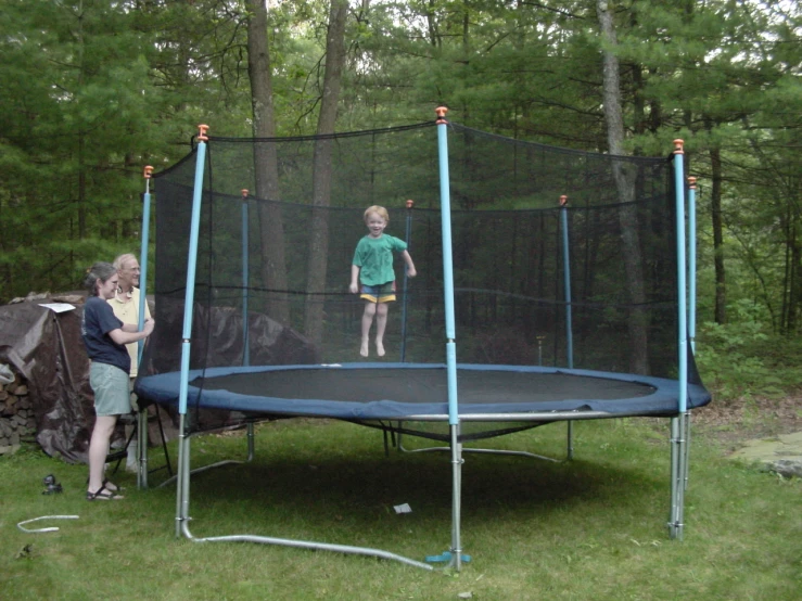 a boy stands on a blue trampoline near two other children