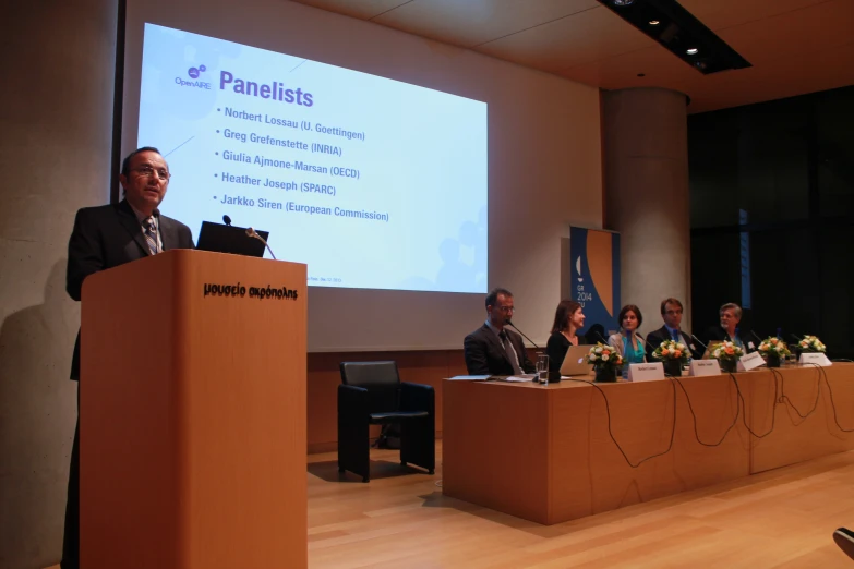 several people are sitting at a podium as a man stands next to a podium