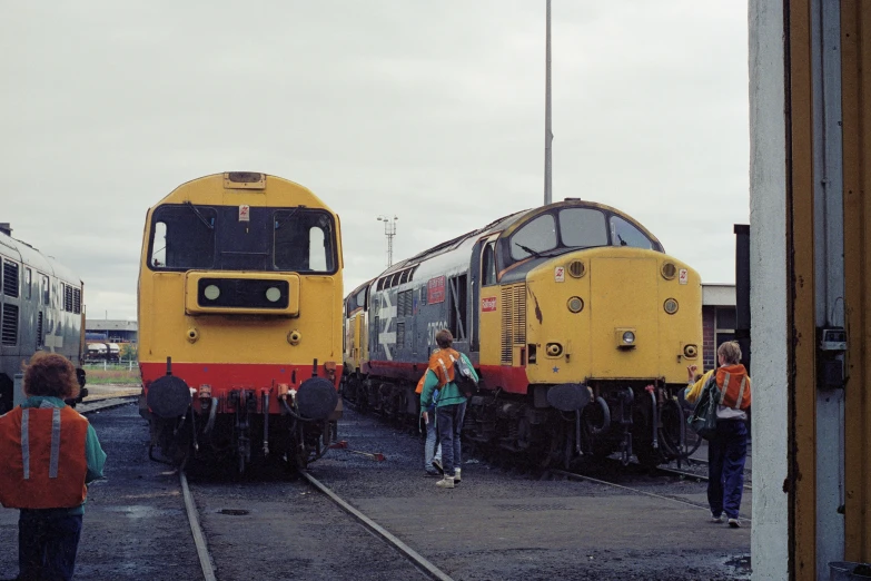 three trains on railroad tracks with some people standing near them