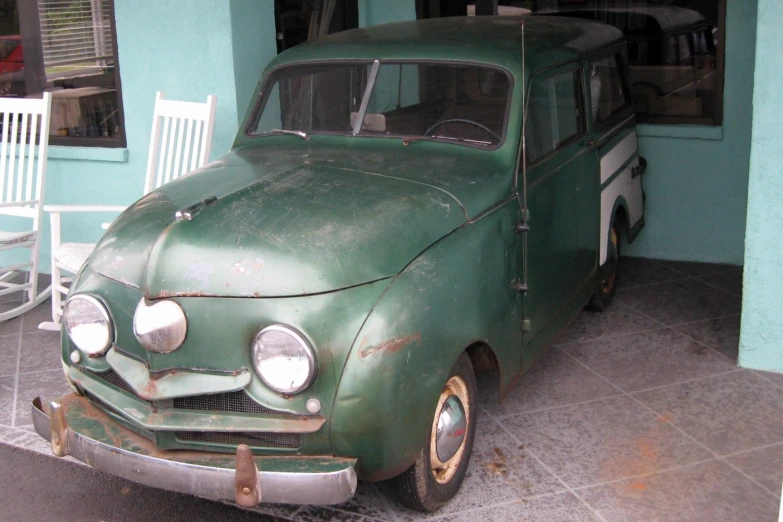 the old green car is parked next to the chairs