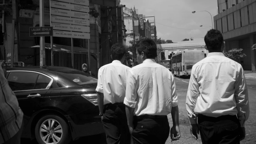 three men walking down the street with a car and bus in background