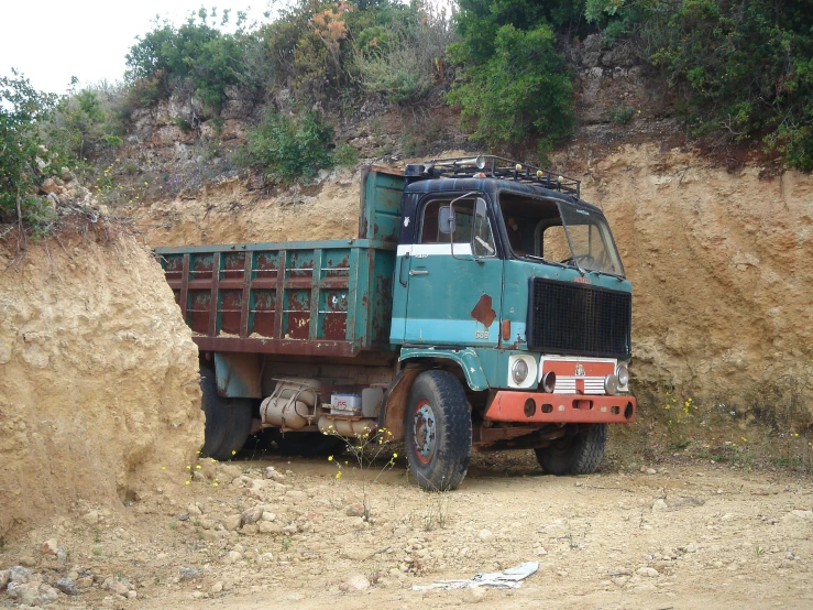 the green dump truck is parked near the mountain