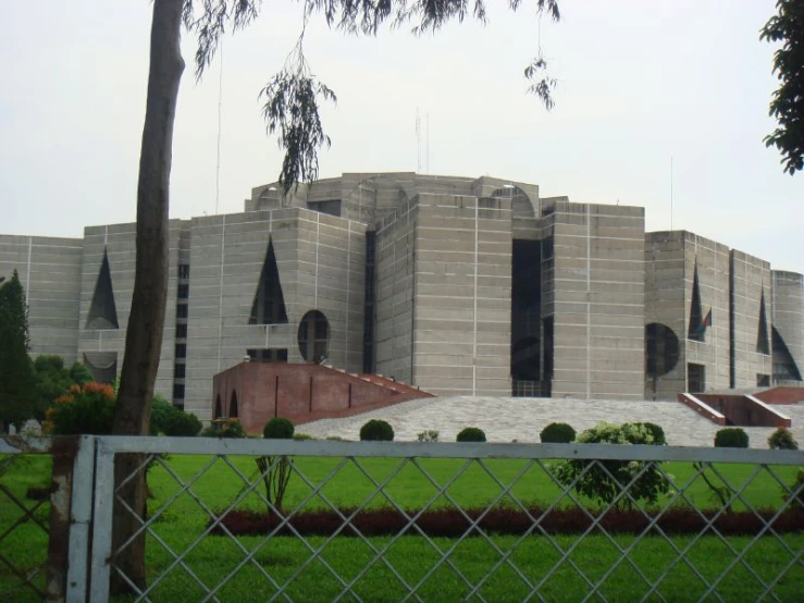 a gray building behind a white fence in front of a lush green field