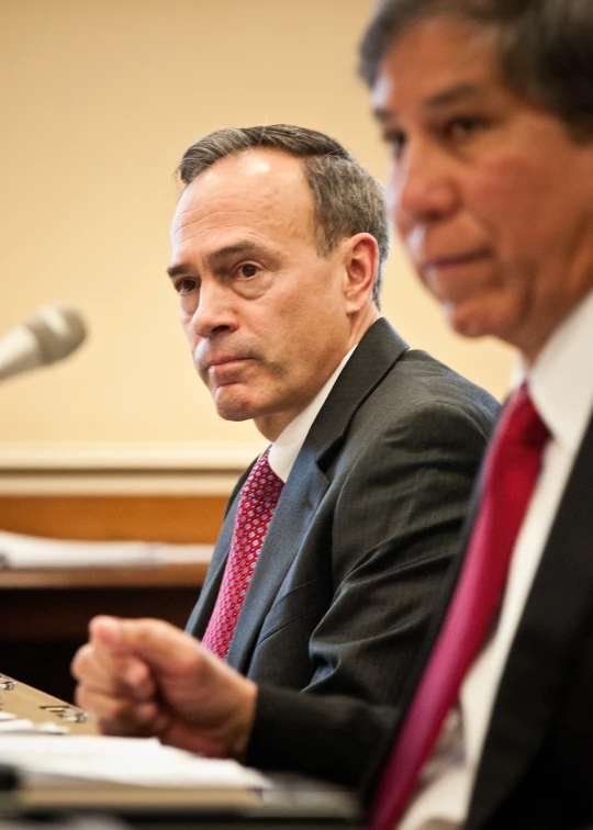 two men in suits and ties sitting at a microphone