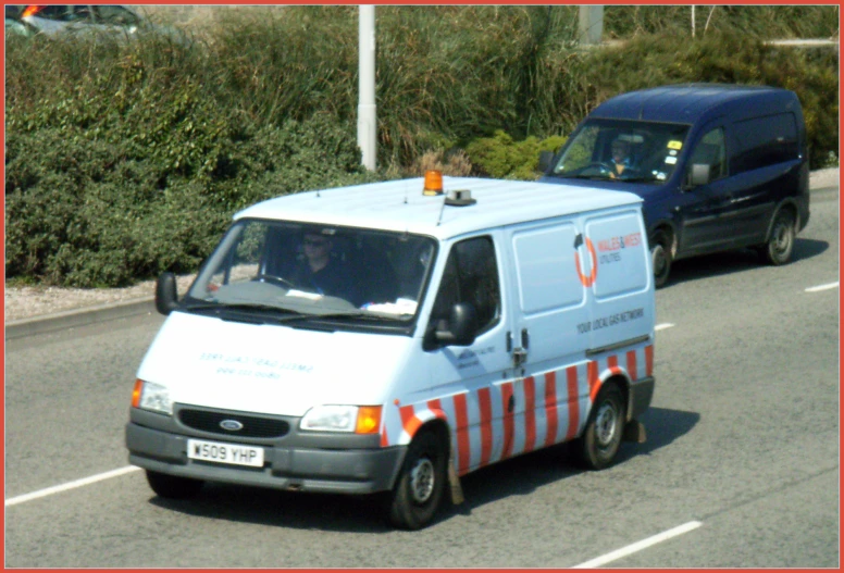 a white van driving down a street past another truck