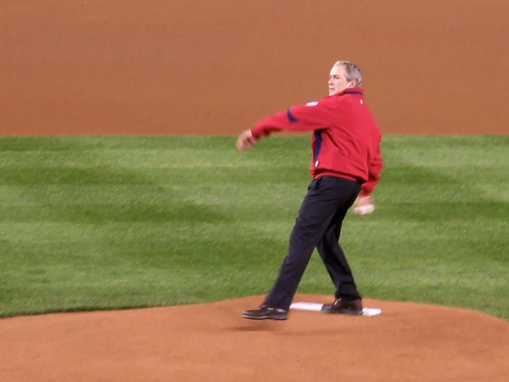 an older man wearing a red jacket tossing a baseball