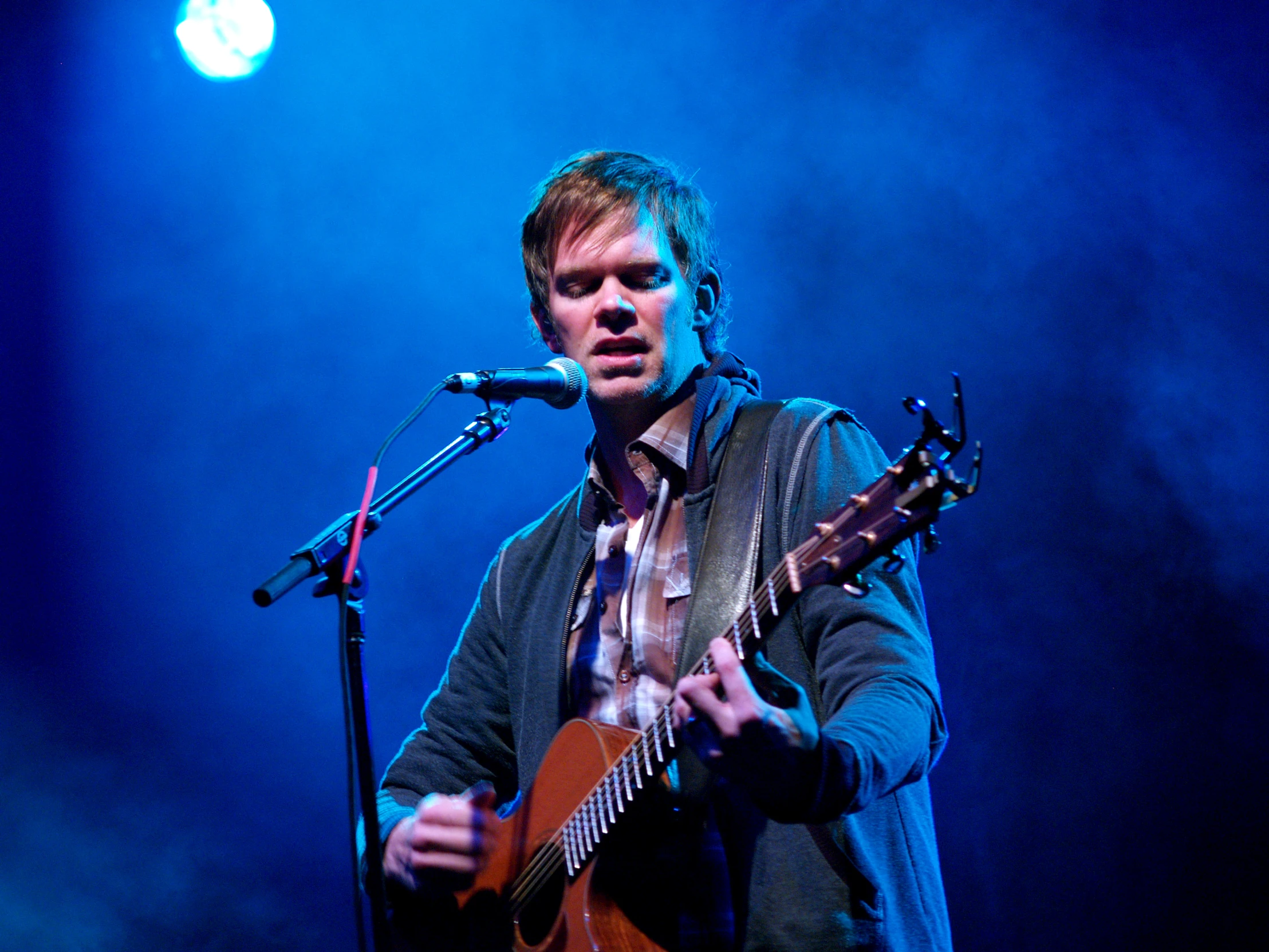 a man on a microphone with an acoustic guitar