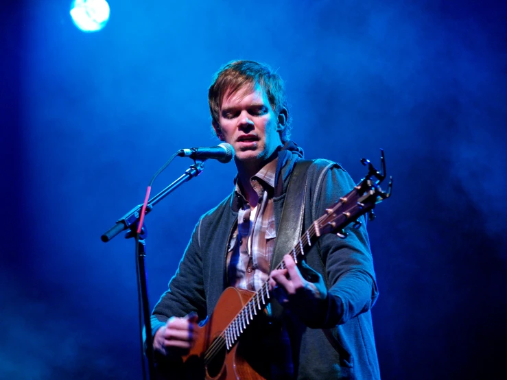 a man on a microphone with an acoustic guitar