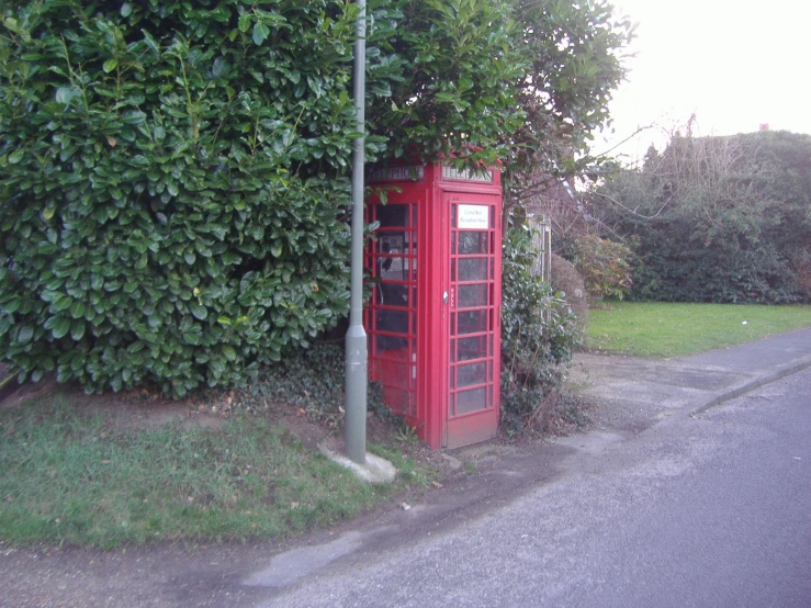 a phone booth is next to a bush and street