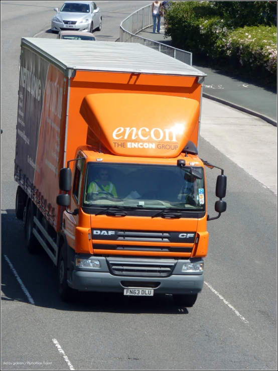 an orange truck driving on the street next to a white car