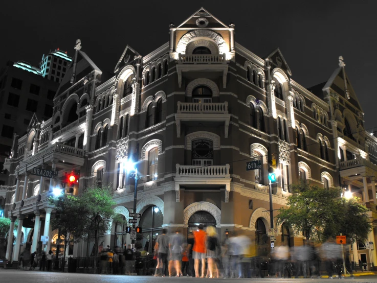 many people are walking down the street in front of an apartment building at night