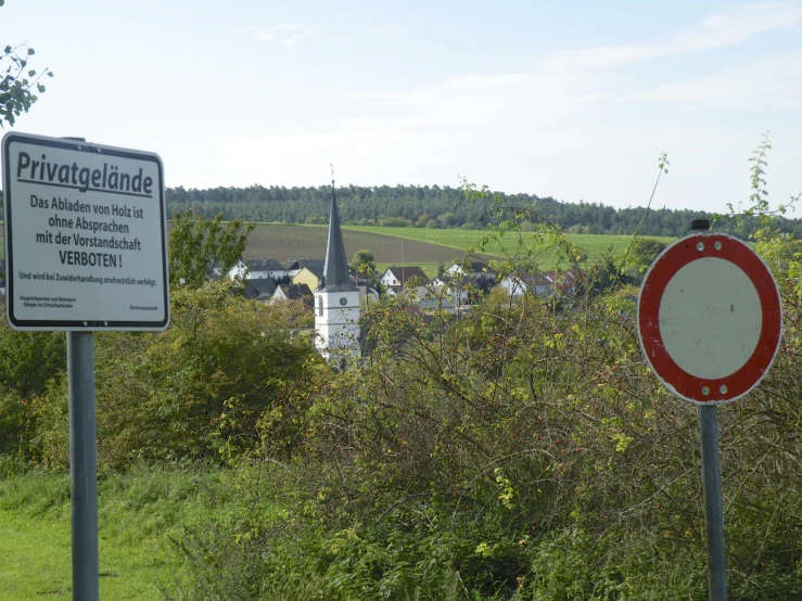 a road sign standing near the grass next to a bush