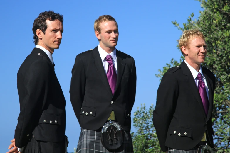 three men are dressed in kilts on a sunny day