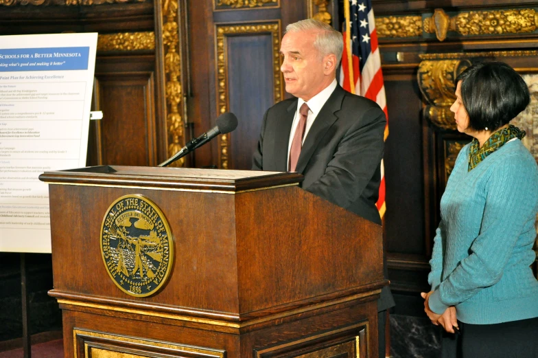 a man and woman stand behind a podium, with an american flag in the background