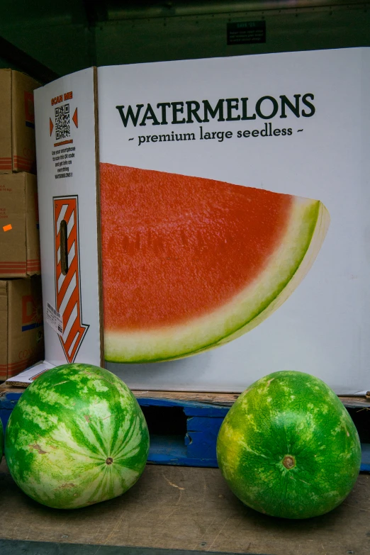 two watermelons sitting in front of a sign next to boxes