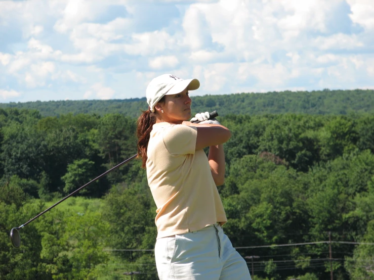 a young person wearing white shorts and a yellow shirt swinging a golf club