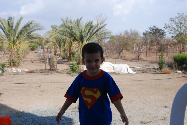 a little  standing on a dirt ground next to palm trees