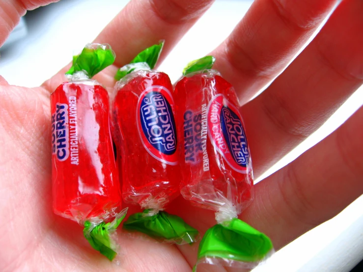 three red drink packets with green leaves on the palm