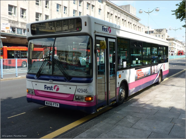 a pink and white commuter bus parked on the side of the street