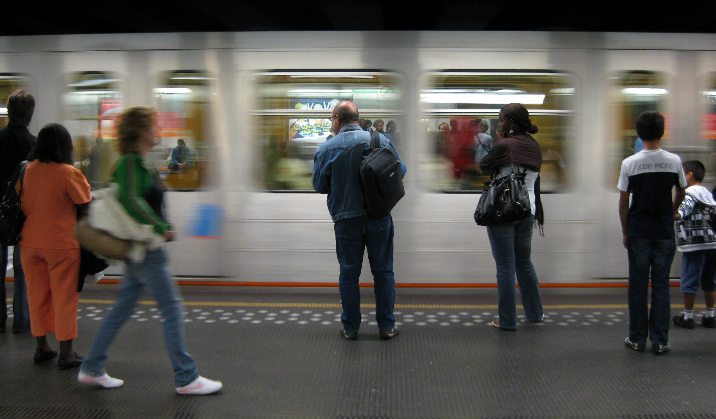 people waiting on a subway train platform as it speeds by