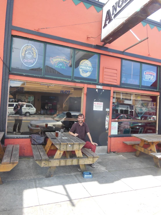 a man sits in a doorway by the picnic tables outside a pizza joint