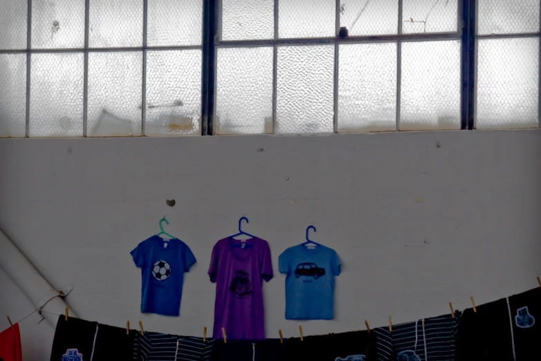 three shirts hung on clothesline against wall with window