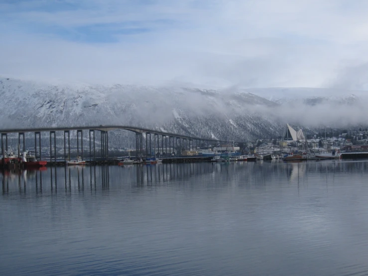 view of the lake and bridge in the city with snow on mountains in the background