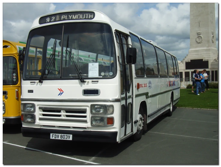 the white bus is parked with people standing near by